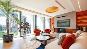 Un salon moderne doté d’un grand téléviseur, de fauteuils rouges, d’un canapé et d’une grande fenêtre donnant sur la ville.