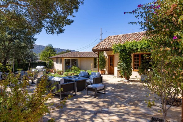 A patio with outdoor furniture, a barbecue grill, and a house with a tiled roof.