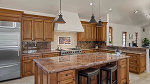 Una cocina con armarios de madera, encimeras de granito, un refrigerador de acero inoxidable y una isla central con taburetes de bar.