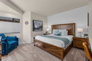 A bedroom with a wooden bed, a blue chair, a bedside table with a lamp, and a wall-mounted picture. - New Listing! Hotel style suite in Mt. Bachelor Village! (Bend)