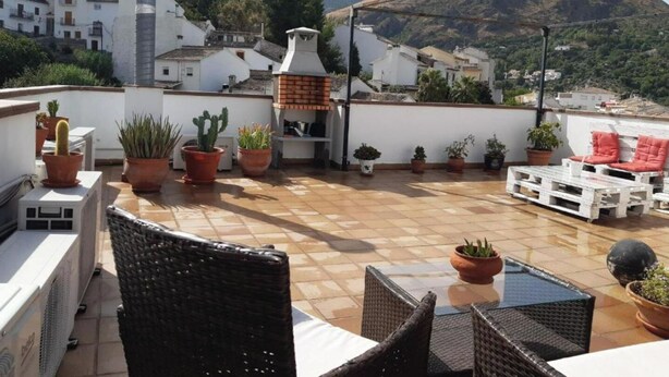 Una terraza en la azotea con plantas en macetas, mobiliario de exterior y vistas de los edificios y montañas circundantes.