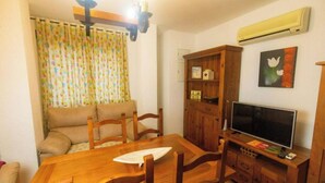 Una sala de estar acogedora con una mesa de comedor de madera, sillas, un sofá, un televisor, un armario y una ventana con cortinas.
