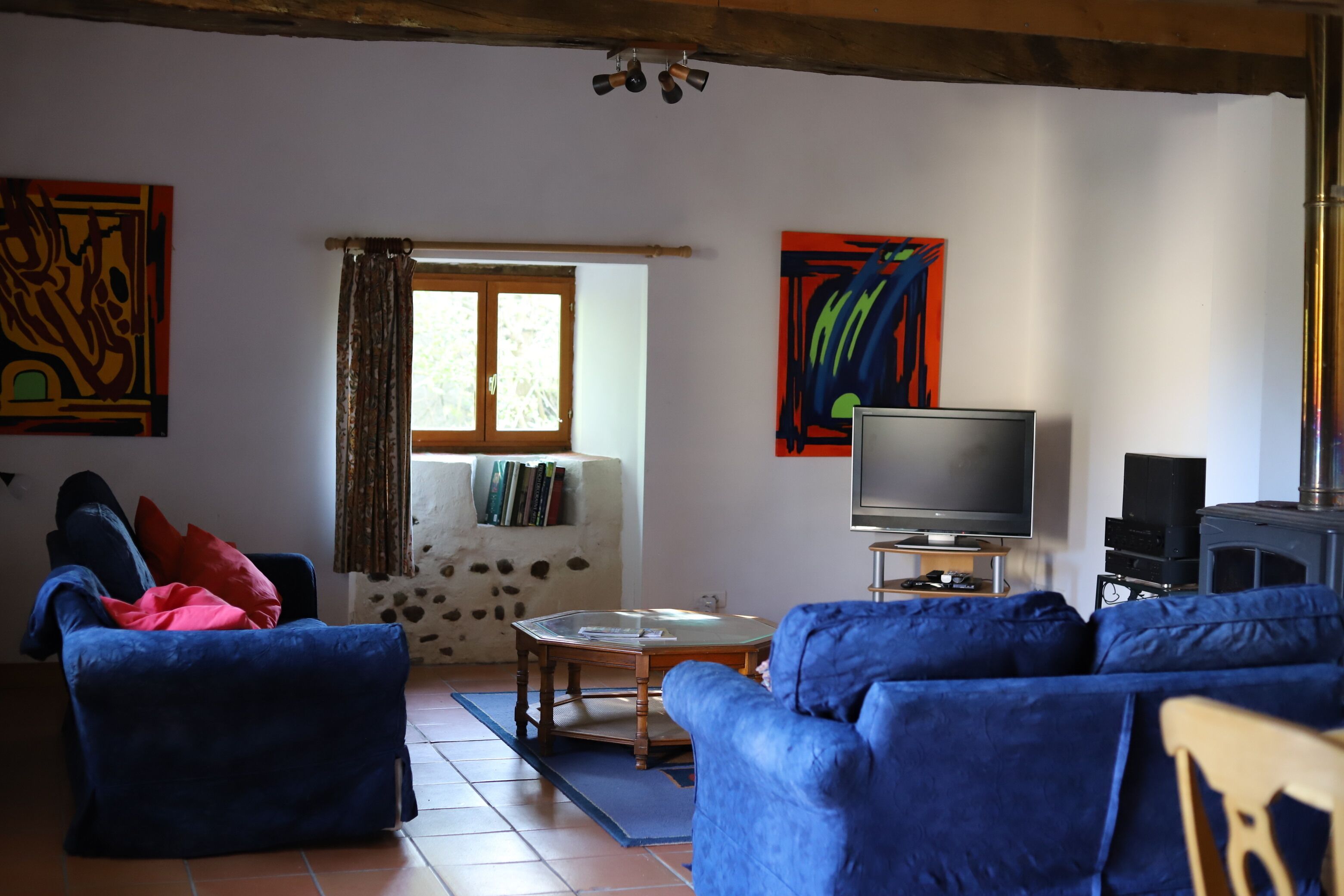 Un salon avec des canapés bleus, un téléviseur, une cheminée et des œuvres d’art accrochées aux murs.