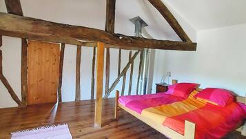 A bedroom with a sloped ceiling, wooden beams, a bed with a colorful blanket, and a wooden floor.