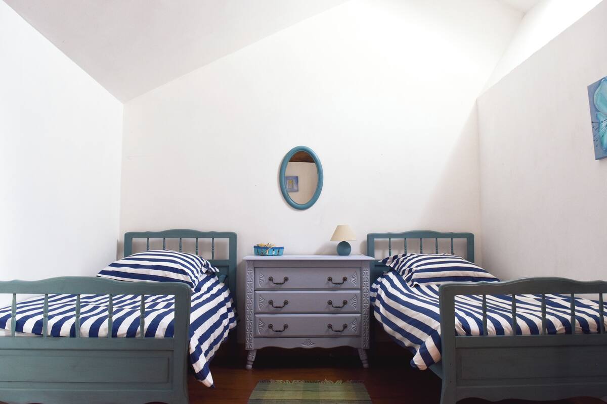 Quarto com duas camas, cômoda, espelho e abajur.
