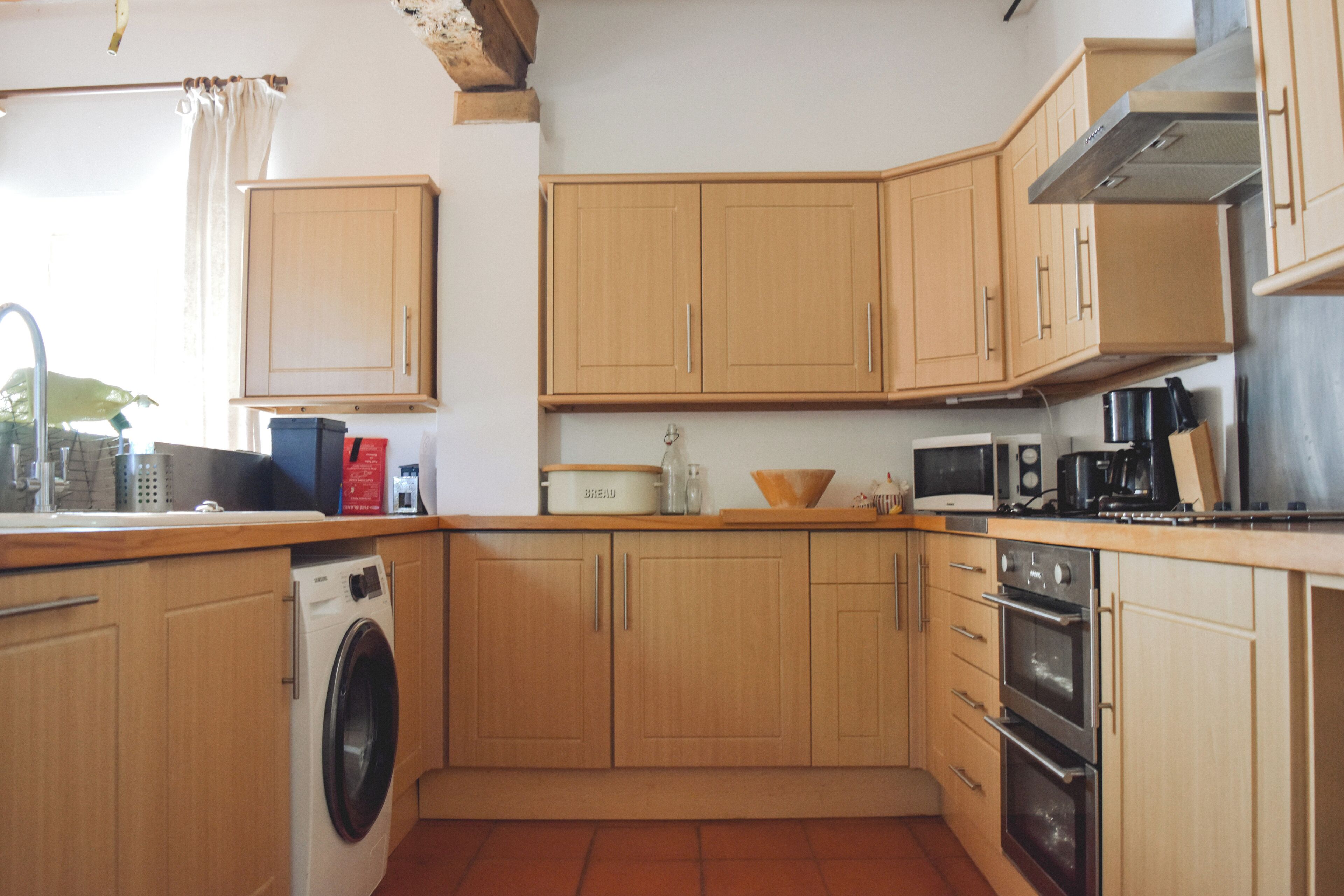 A compact kitchen with wooden cabinets, a washing machine, a microwave, and a coffee maker.