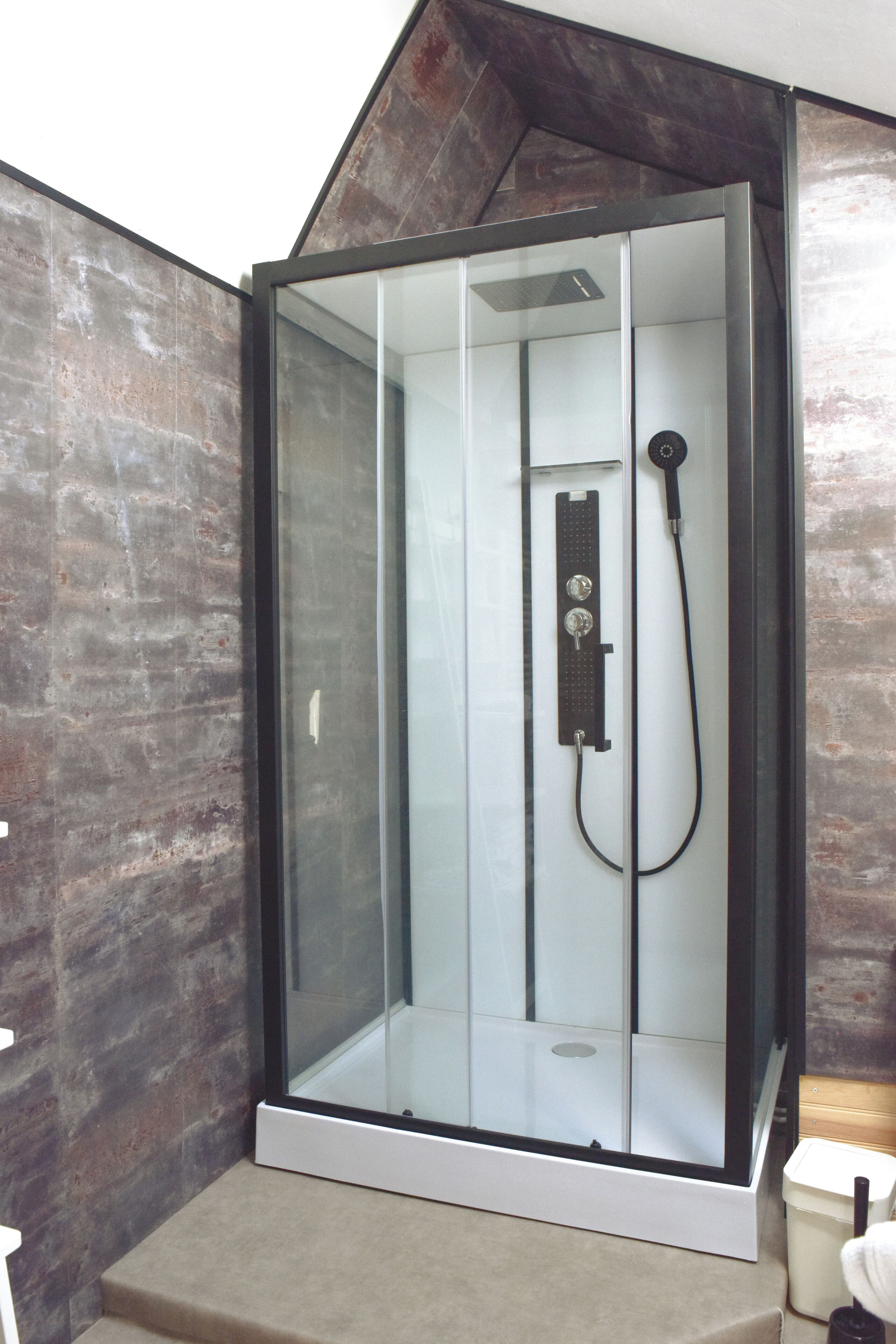 Une cabine de douche moderne dotée d’une porte en verre, d’un pommeau de douche à main et d’un panneau de commande.