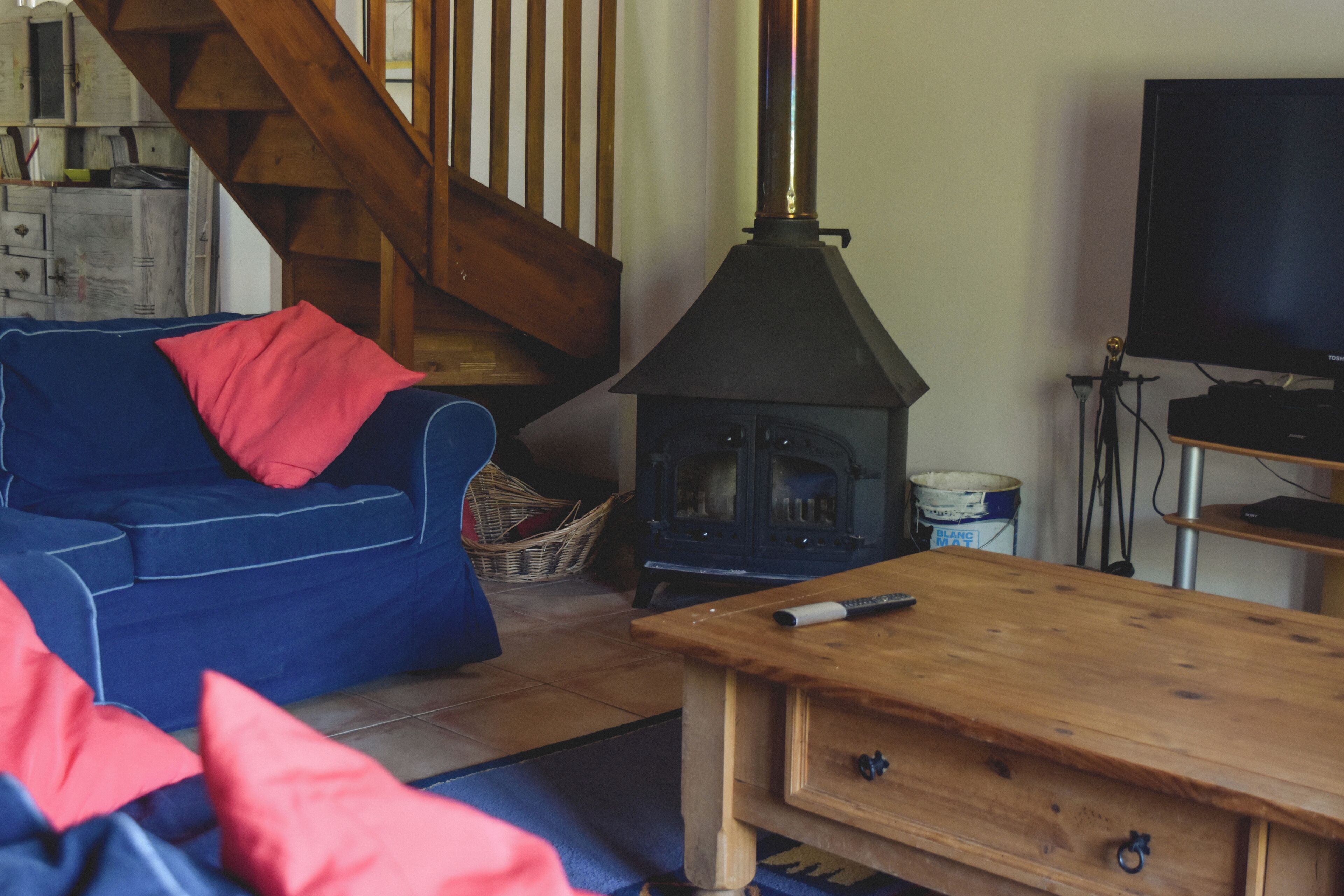 Ein gemütliches Wohnzimmer mit einem blauen Sofa, roten Kissen, einem Holztisch, einem Kamin, einem Fernseher und einer Treppe.