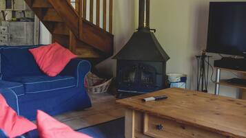 Ein gemütliches Wohnzimmer mit einem blauen Sofa, roten Kissen, einem Holztisch, einem Kamin, einem Fernseher und einer Treppe.