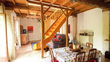 A rustic interior with a wooden staircase, a dining area with a table and chairs, and a living room with a sofa and television.