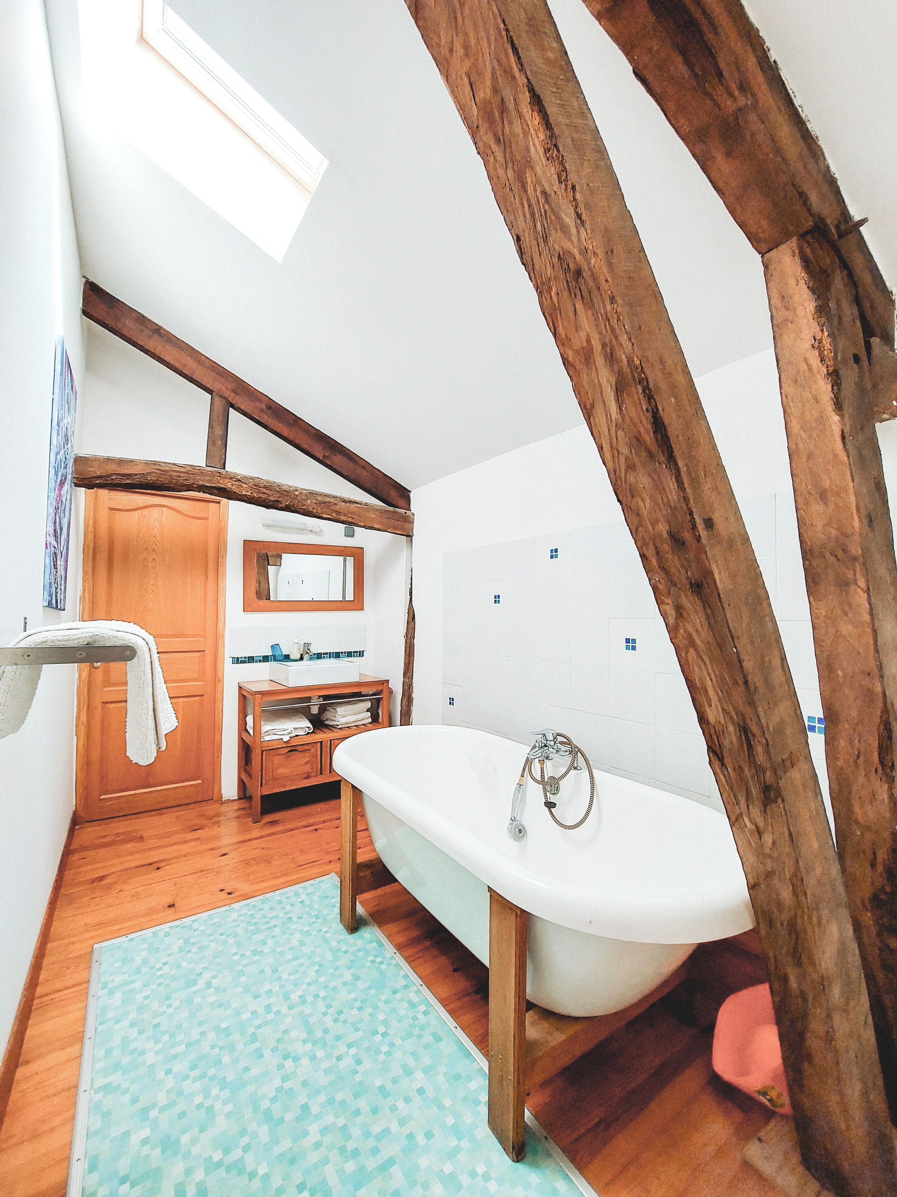 Un baño con piso de madera, una bañera blanca, un tocador de madera y una puerta de madera.