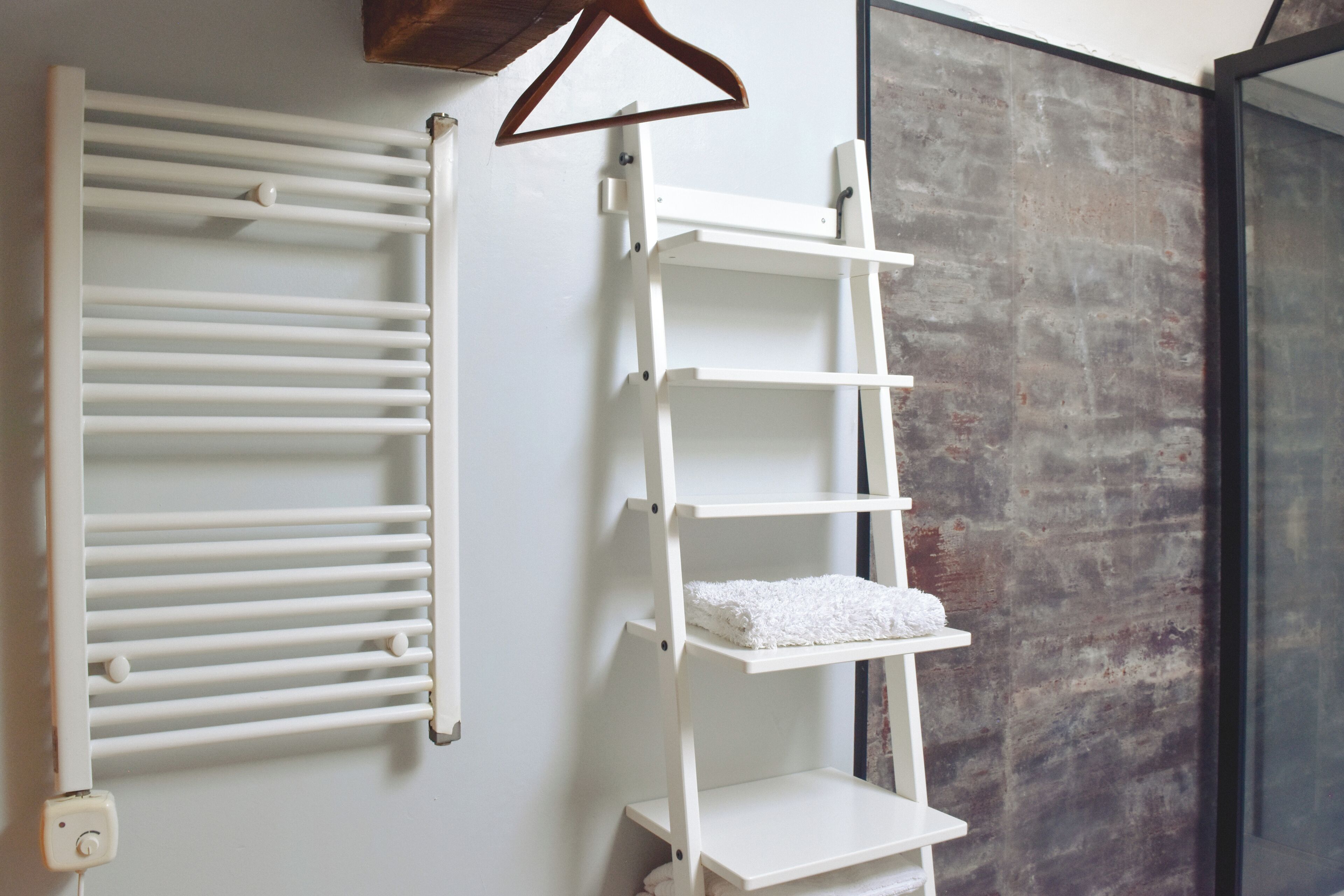 A bathroom with a white towel rack, a white shelf with towels, and a textured wall.