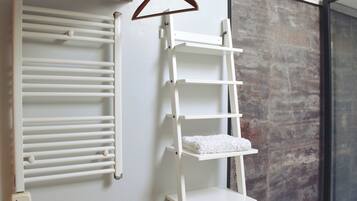 A bathroom with a white towel rack, a white shelf with towels, and a textured wall.