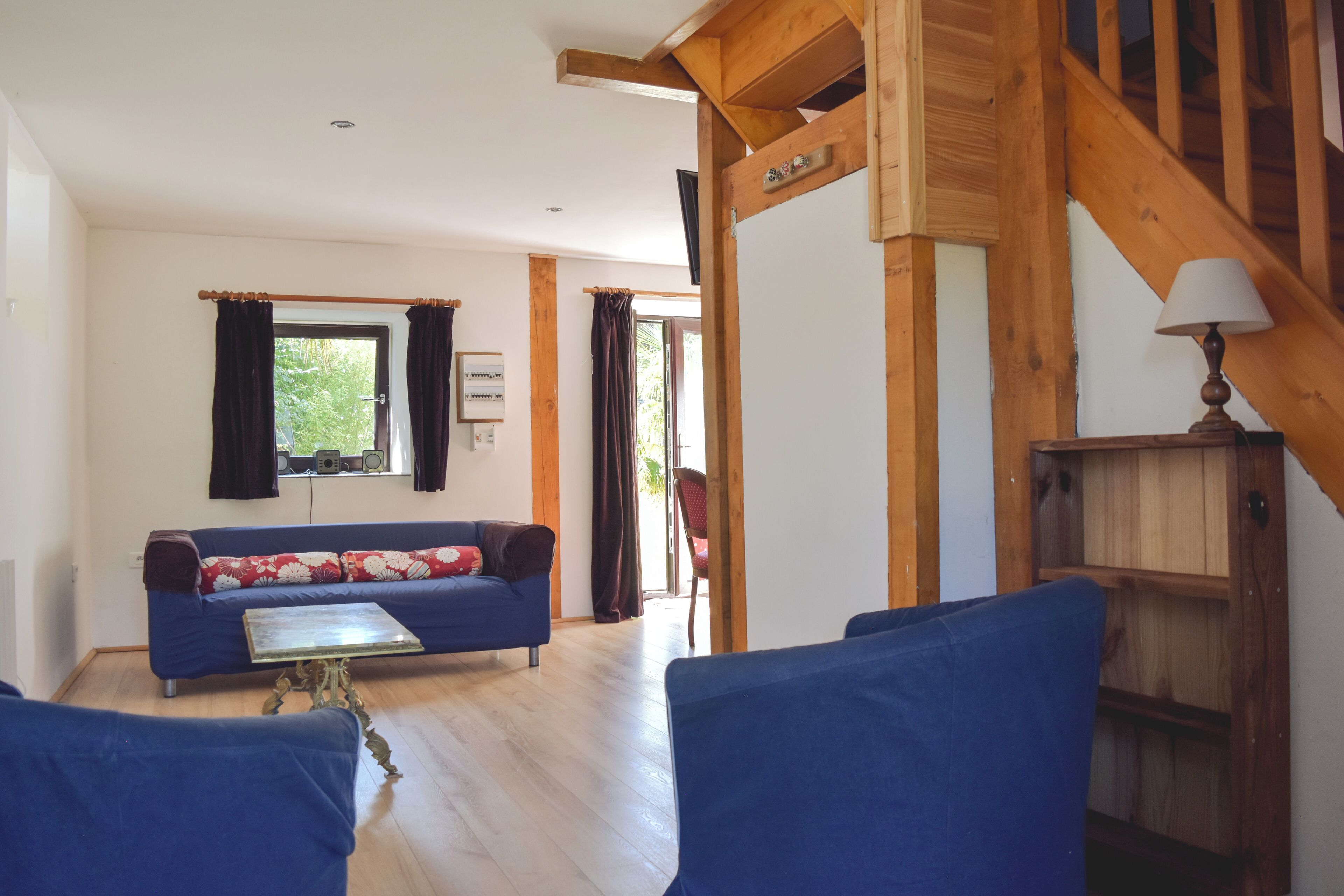Una sala de estar con un sofá azul, vigas de madera, una escalera y un armario de madera.