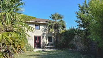 Une maison avec une porte rouge, une petite fenêtre et une terrasse avec une table et des chaises.