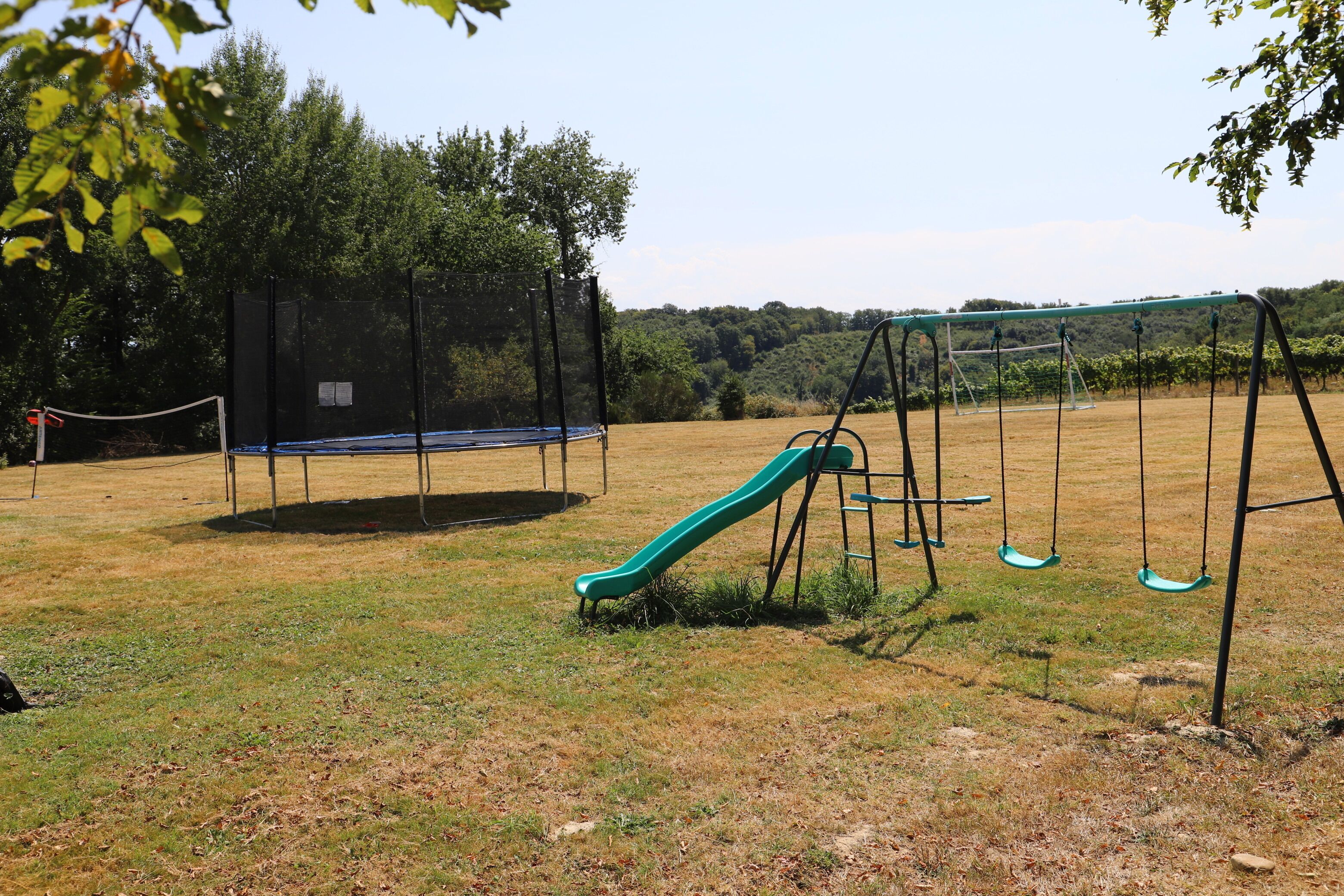 Ein Spielplatz mit Rutsche und Schaukeln, umgeben von Bäumen und Gras.