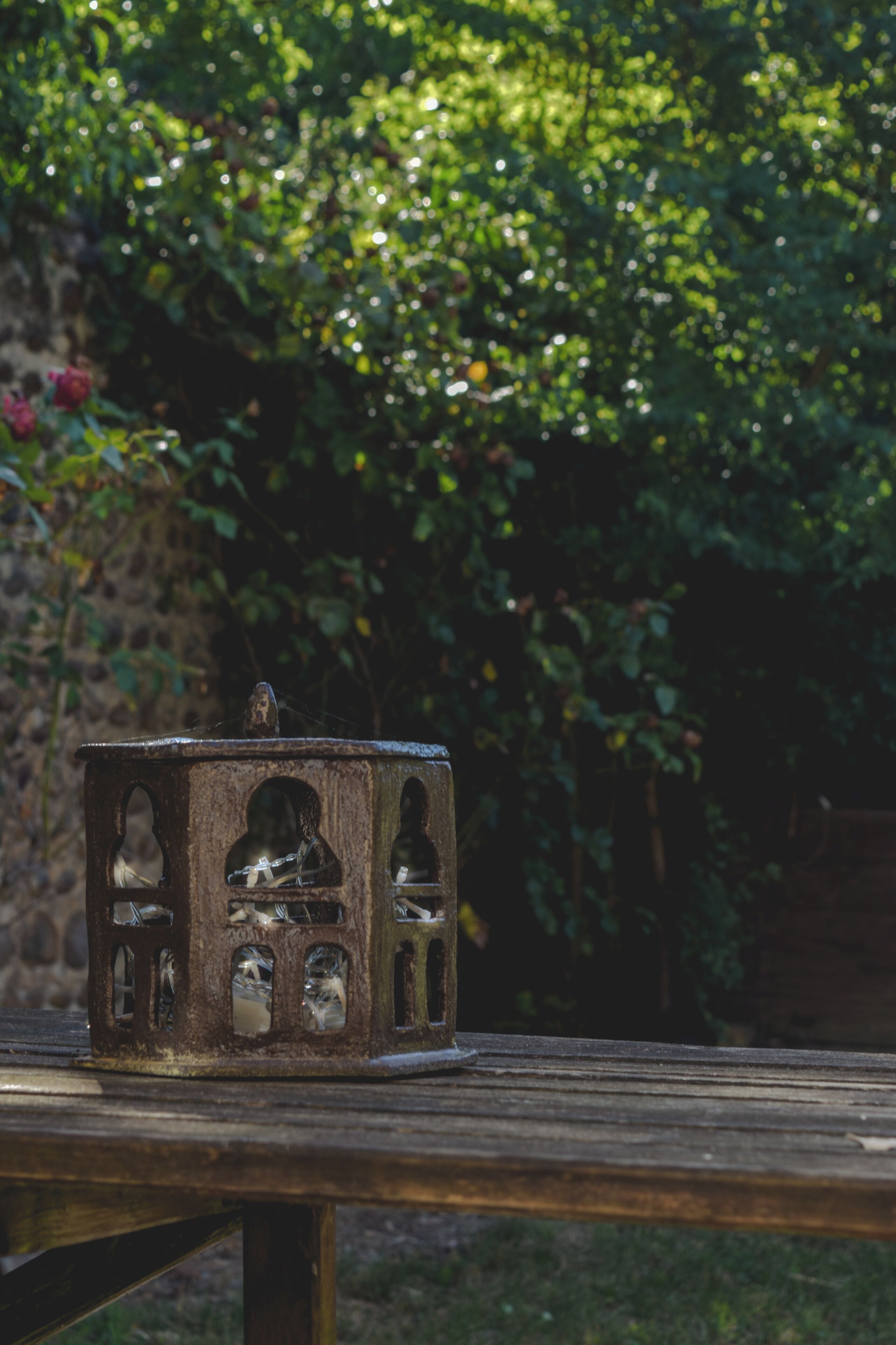 A rustic metal lantern with multiple openings and a spider web on top, placed on a wooden surface.