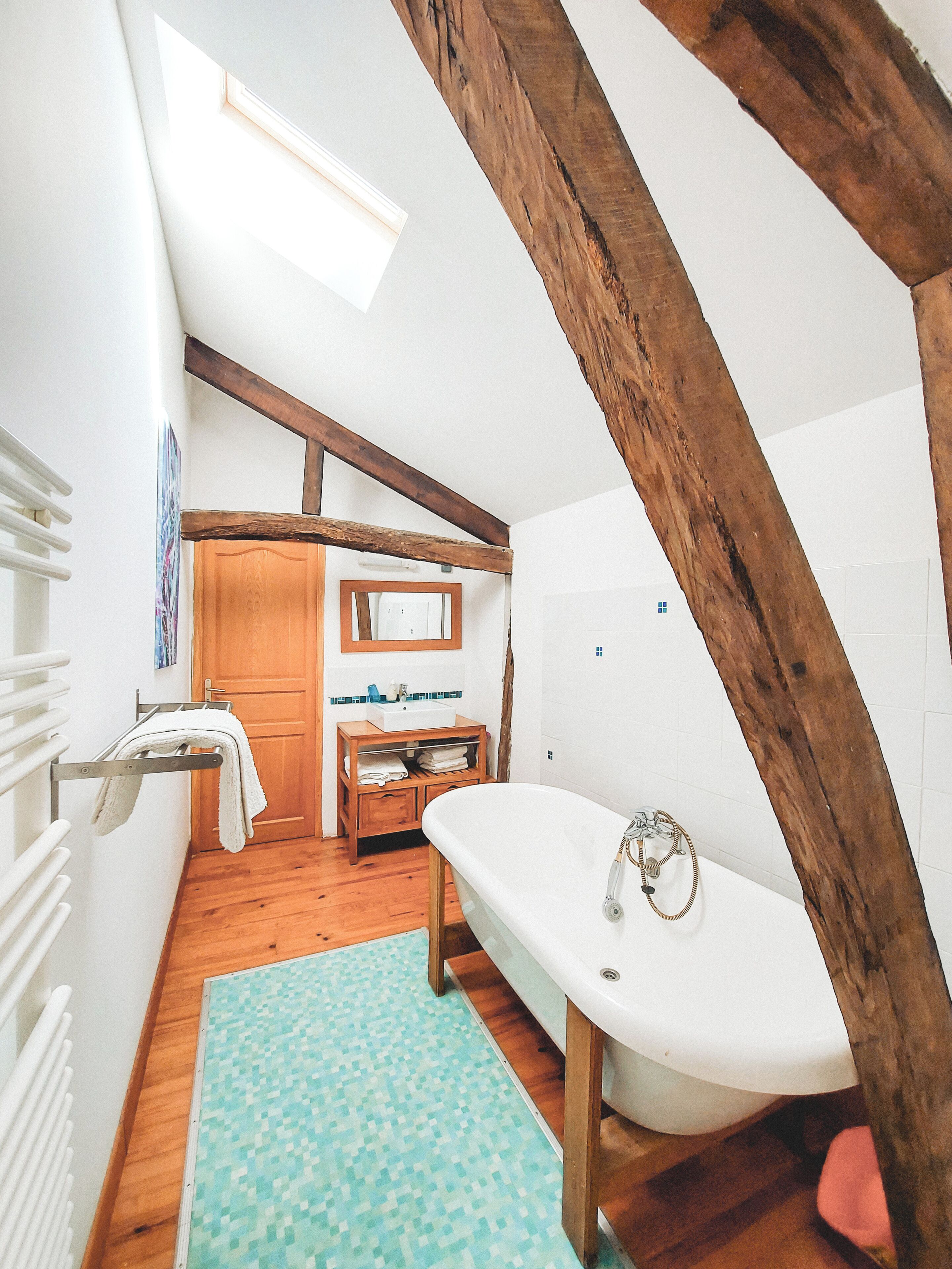 A small, rustic bathroom with a wooden ceiling, a white bathtub, a wooden vanity, and a tiled floor.