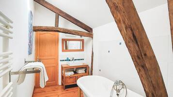 A small, rustic bathroom with a wooden ceiling, a white bathtub, a wooden vanity, and a tiled floor.