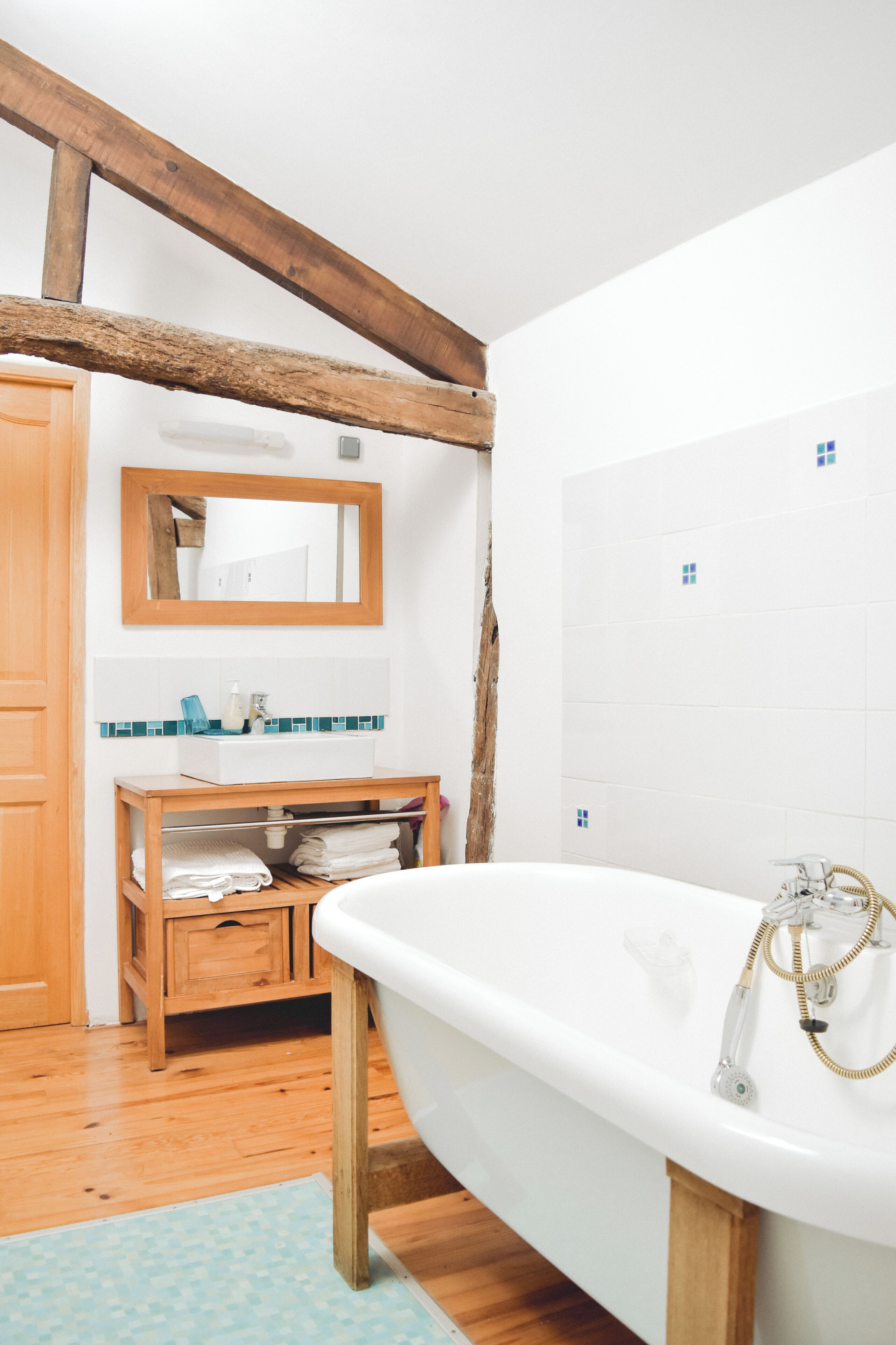 A bathroom with a wooden vanity, a white bathtub, and a tiled wall.