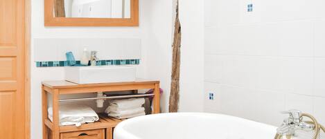 A bathroom with a wooden vanity, a white bathtub, and a tiled wall.