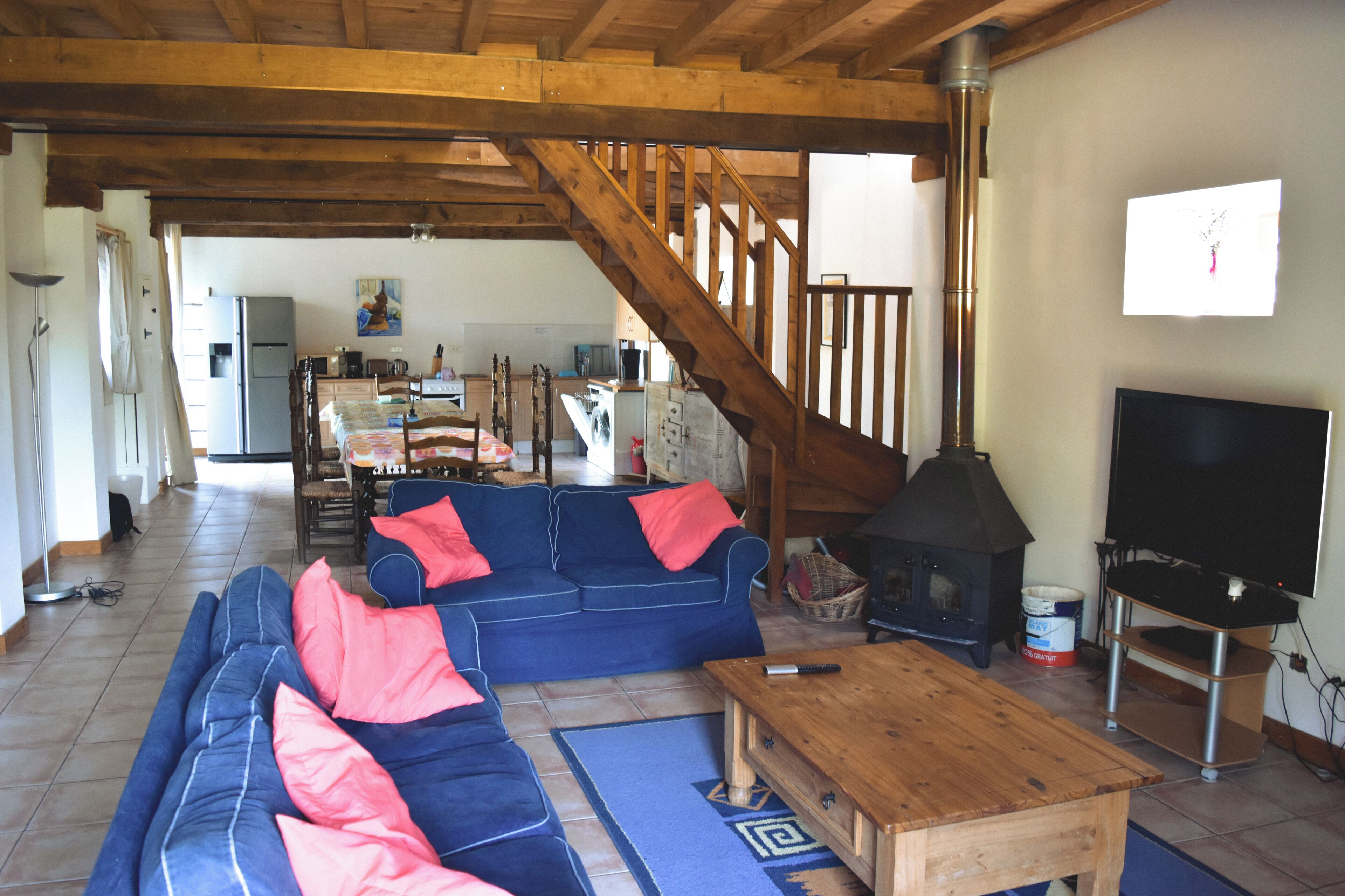 Un salon spacieux avec un canapé bleu, une table basse en bois et un téléviseur. Un escalier mène à l’étage supérieur.