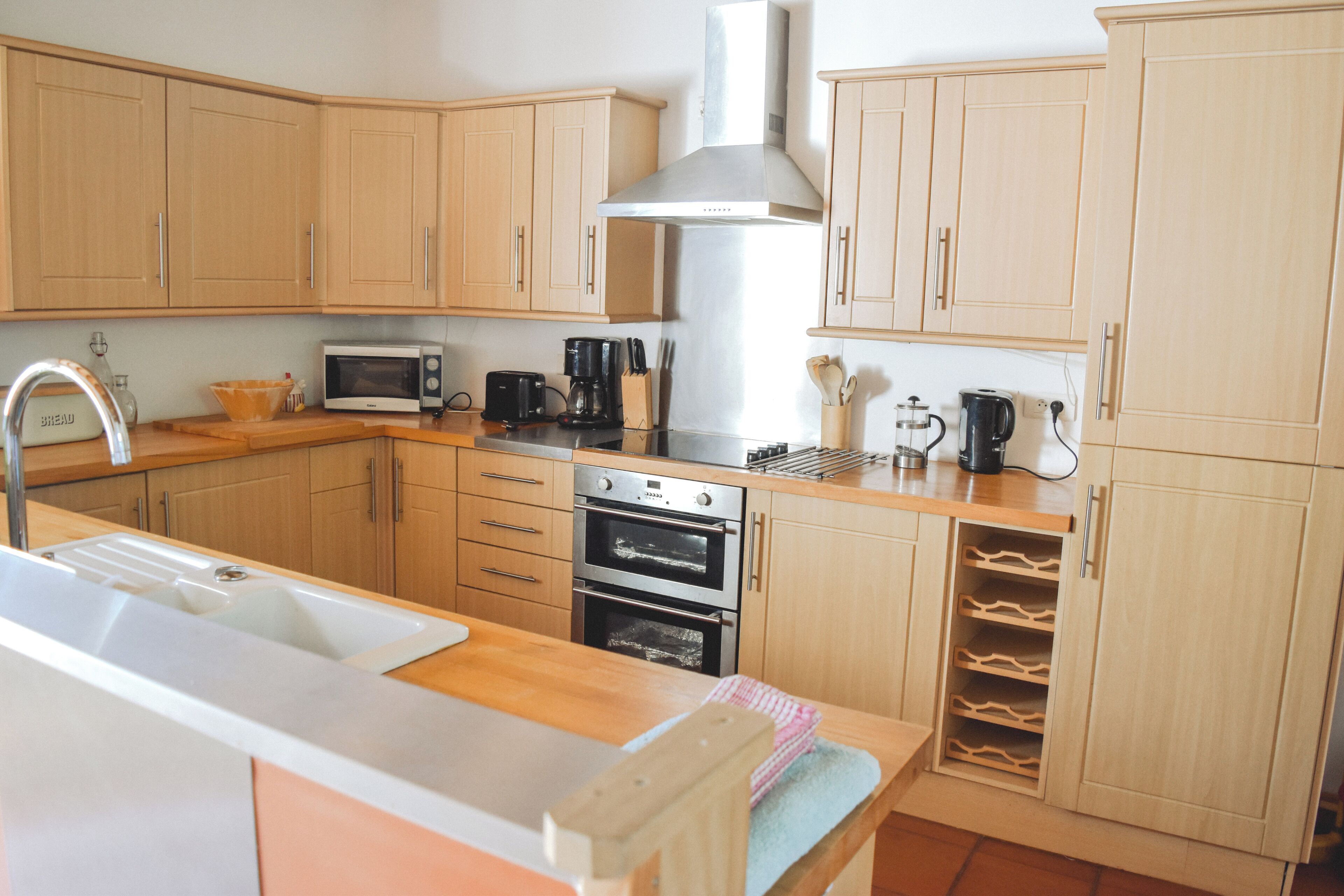 Una cocina con armarios de madera, una campana extractora de acero inoxidable, un microondas, una cafetera y una estantería para vinos.