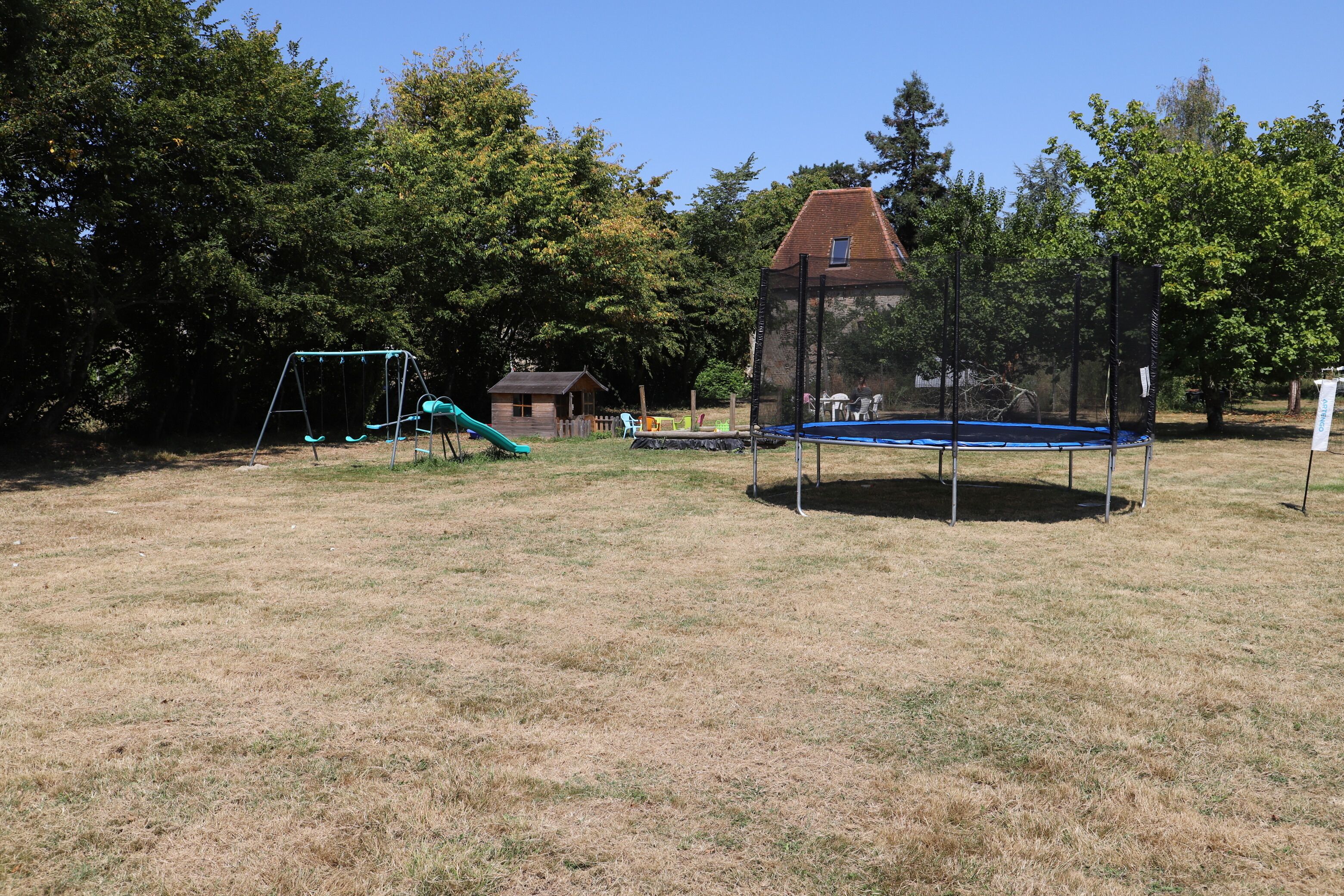 Un parque infantil con columpios, tobogán, trampolín y una zona vallada.