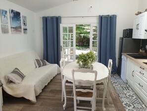 Un salon chaleureux avec un canapé blanc, une table à manger avec des chaises et un coin cuisine équipé de placards et d’un réfrigérateur.