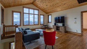 A spacious living room with a high ceiling, large windows, a TV, and a red chair.