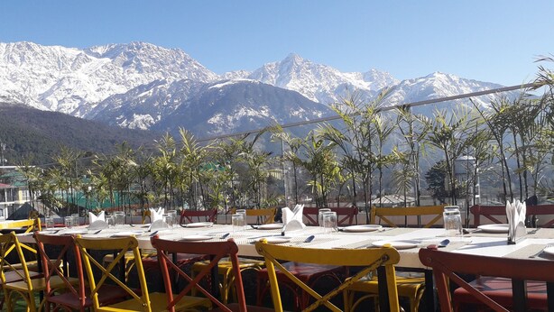 A restaurant with tables and chairs, a mountain view, and some greenery in the foreground. - Hotel Centre Point (Dharamshala)