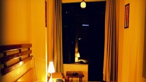 A hotel room with a bed, a nightstand, a lamp, and a window with curtains. - Hotel Centre Point (Dharamshala)