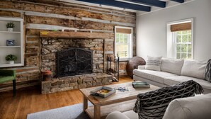 A cozy living room with a stone fireplace, a white sofa, and a wooden coffee table. - Walk to Old Rag | Hot Tub | Dog-Friendly Farmhouse (Sperryville)