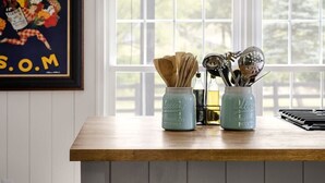 A kitchen with a wooden island, white cabinets, and a window with a view of trees. There is a framed poster on the wall and a jar with utensils on the island. - Walk to Old Rag | Hot Tub | Dog-Friendly Farmhouse (Sperryville)
