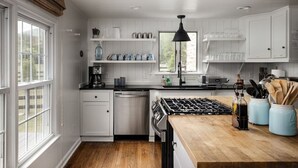 A modern kitchen with white cabinetry, a wooden countertop, and a gas stove. - Walk to Old Rag | Hot Tub | Dog-Friendly Farmhouse (Sperryville)