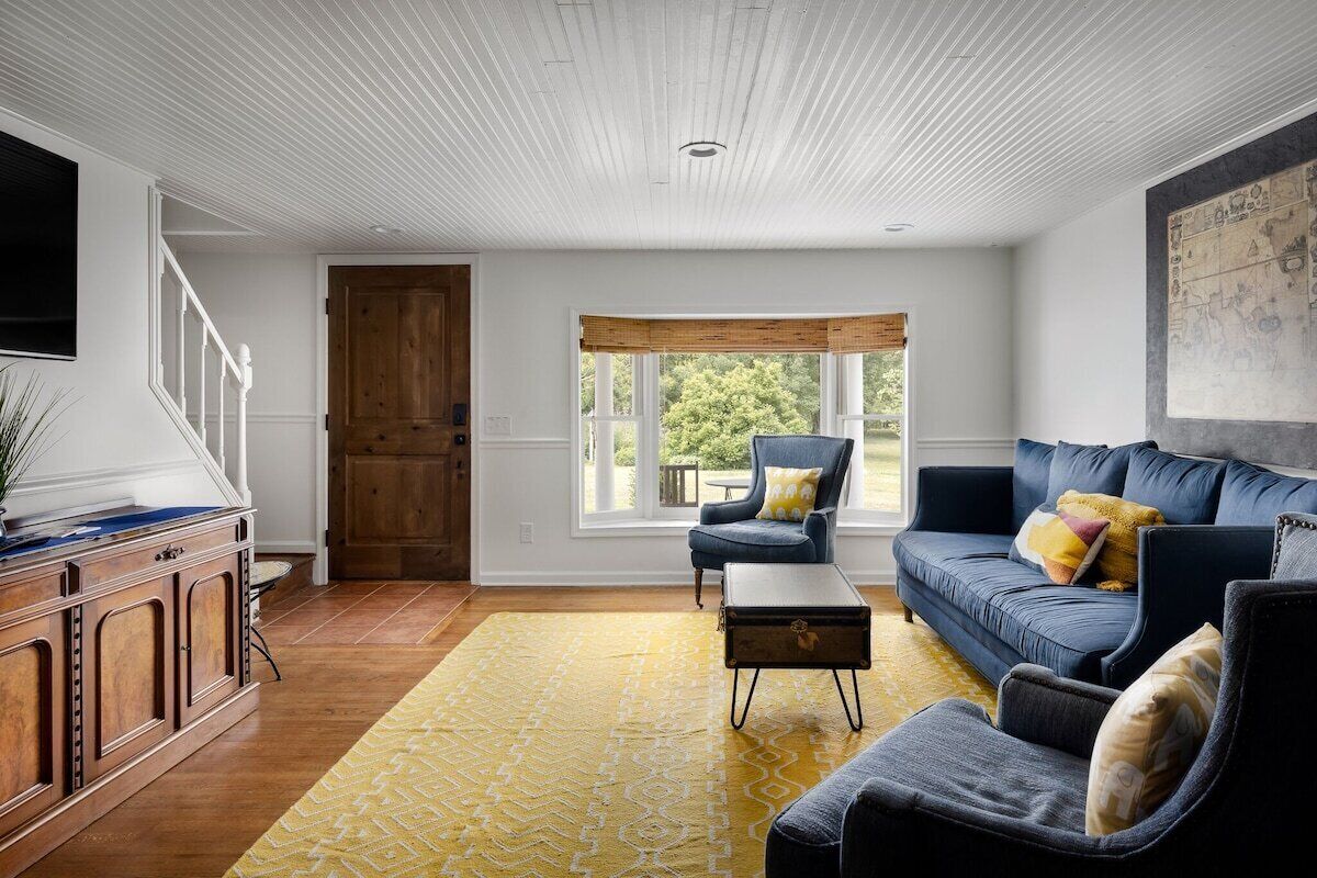 Una sala de estar con un mueble de madera, un sofá azul y un tapete amarillo estampado.