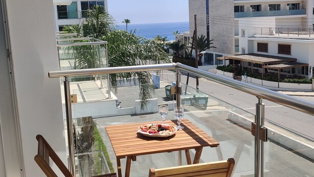 A balcony with a wooden table and chairs, a bowl of fruit, and a glass of water. - Charming 1-bed Apartment in Protaras, Cyprus (Paralimni)