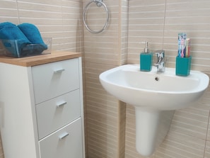 A bathroom with a white sink, two blue toothbrush holders, and a wooden cabinet with two towels. - Charming 1-bed Apartment in Protaras, Cyprus (Paralimni)