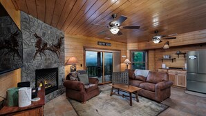 Interior acogedor de una cabaña con chimenea de piedra, sofás de cuero, comedor y cocina.