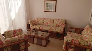 A living room with a floral sofa, two armchairs, and a glass coffee table.