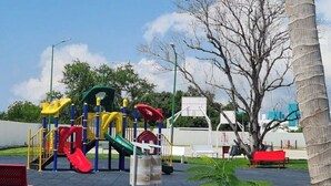 Ein Spielplatz mit Rutschen, Klettergerüsten, einer Bank und einer Palme.