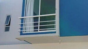 Ein modernes Gebäude mit einer blauen und weißen Fassade, einer schwarzen Tür und einem Fenster mit weißem Rahmen und Vorhängen.