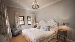 A bedroom with a large bed, a chair, a nightstand, a chandelier, and floral curtains.