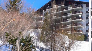 Um edifício com várias andares e varandas, rodeado por árvores e neve.