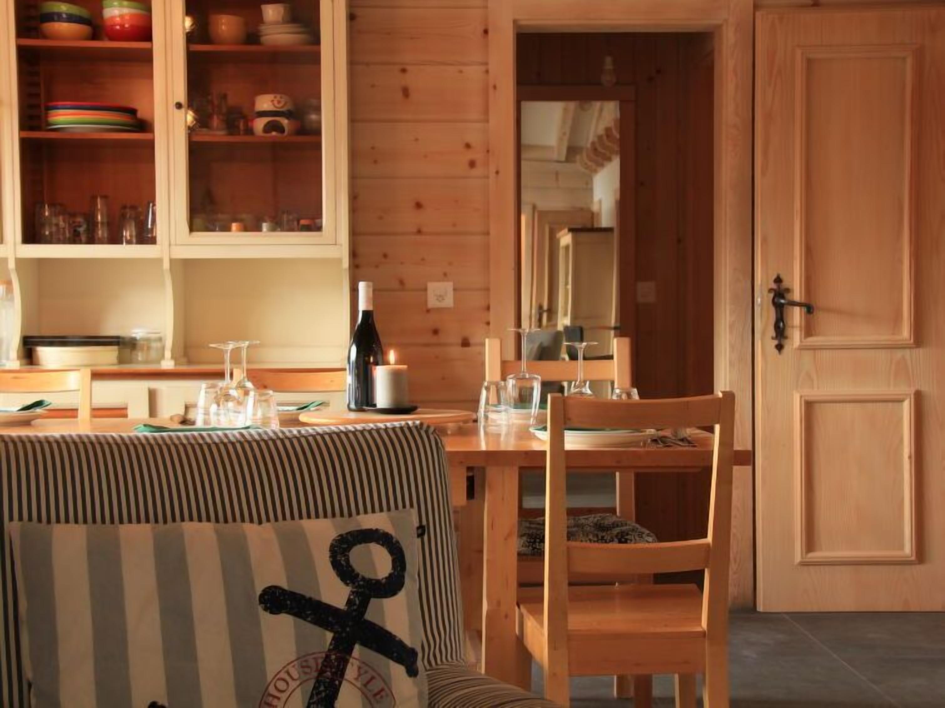 A wooden dining table with chairs, a candle, and a bottle of wine.