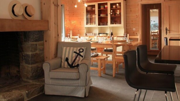 A cozy cabin interior with a stone fireplace, striped armchair, dining table, and wooden cabinets. - Muscardin 5/6 by Interhome (Villars)