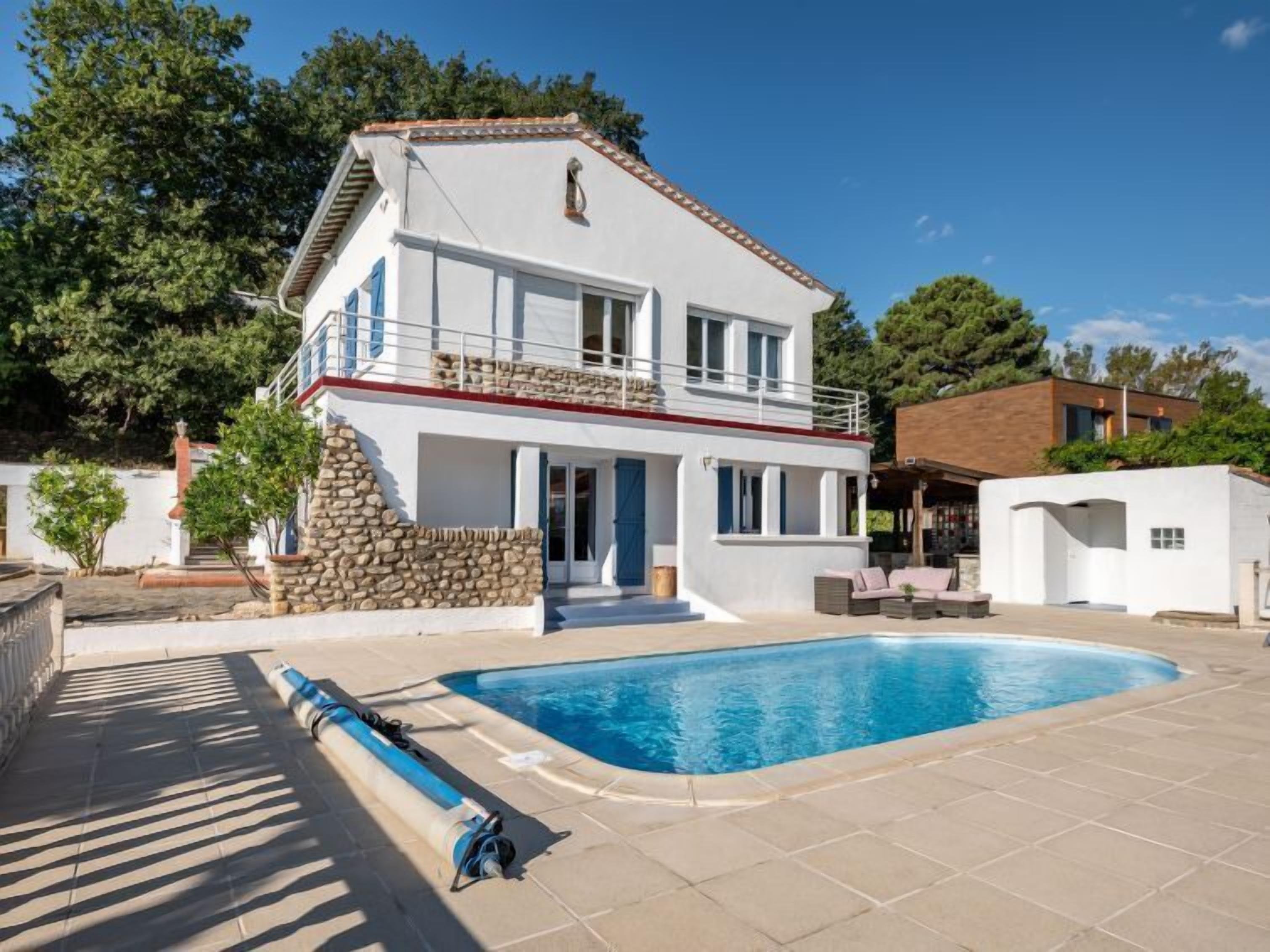 A two-story house with a swimming pool, stone wall, and a covered outdoor area.