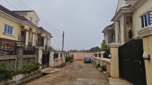 A residential street with houses on both sides, a dirt path, and a parked car. - Smart 3 bed Apartment With Fast Wi-fi & 24hr Light (Abuja)