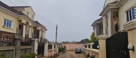 A residential street with houses on both sides, a dirt path, and a parked car.