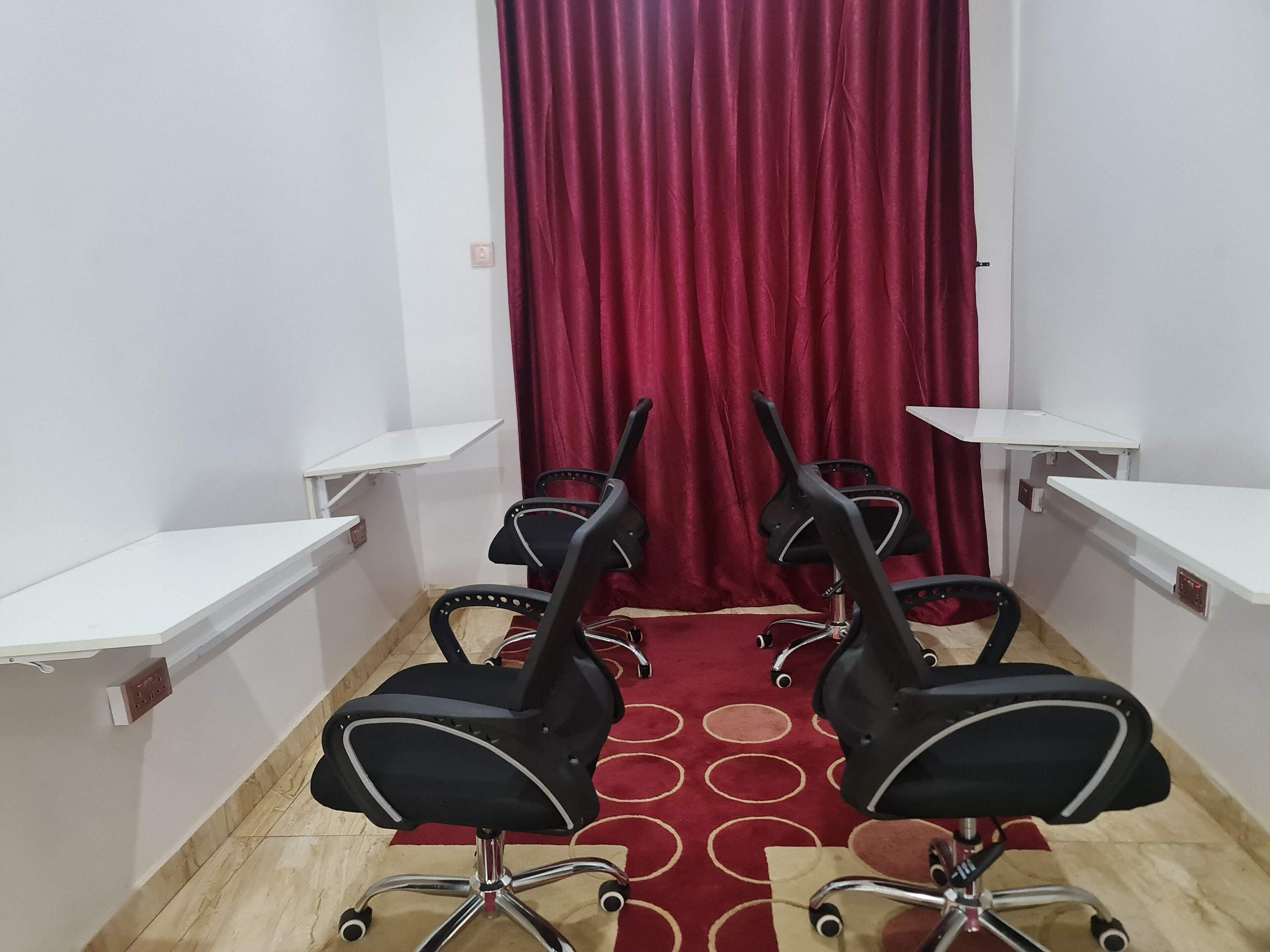 A conference room with four black office chairs, white desks, and a red curtain.